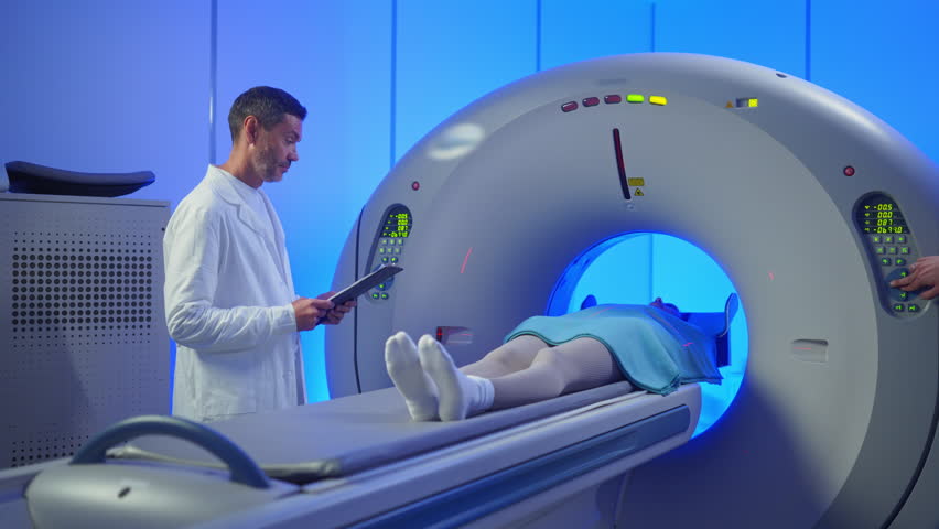 Medical worker standing confidently near MRI tunnel while female patient resting on table. Overseeing post-scan procedure inside professional medical imaging center. Patient lying on CT, PET, or MRI