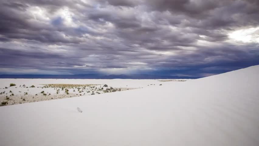 Dramatic clouds hover above the stark dunes of White Sands National Park, highlighting vast gypsum desert under shifting light.