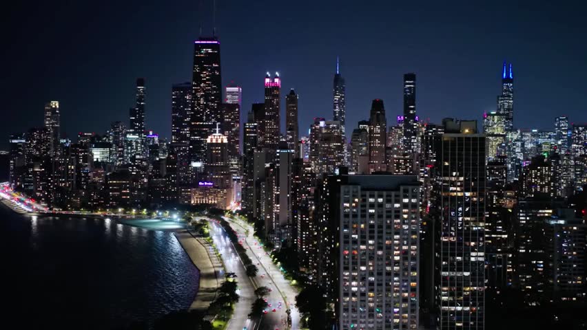 Chicago skyline glows with vibrant city lights at night along Lake Michigan, reflecting urban beauty on calm water.