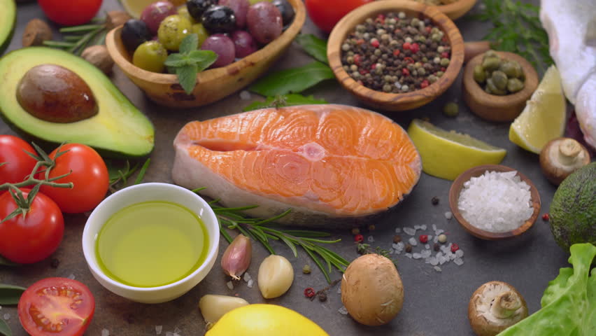 Top view rotating shot of raw salmon, avocado, cherry tomatoes, olives, lemon, olive oil and spices on a wooden board.  Concept of healthy Mediterranean diet and healthy food.