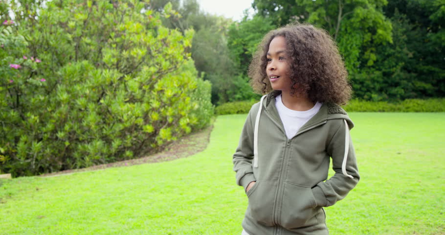 Elementary school boy in hoodie on backyard observing hedge turning to camera, smiling to greet. Outdoor, youth, leisure, nature, casual, childhood, happiness