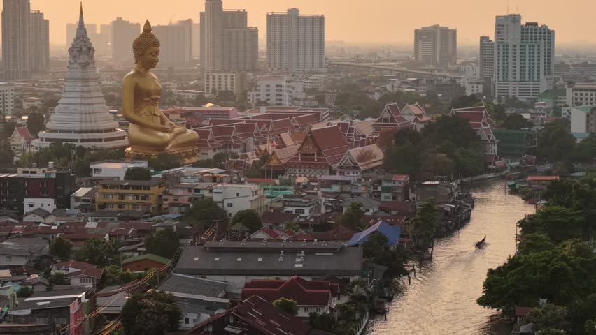 Aerial view Sunset light of the giant gold buddha in Wat Paknam Phasi Charoen Temple in Phasi Charoen district on Chao Phraya River with traditional boat, Bangkok, Thailand. Downtown City.
