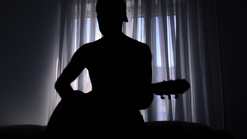 In a dark room, a man plays the guitar masterfully and moves very energetically