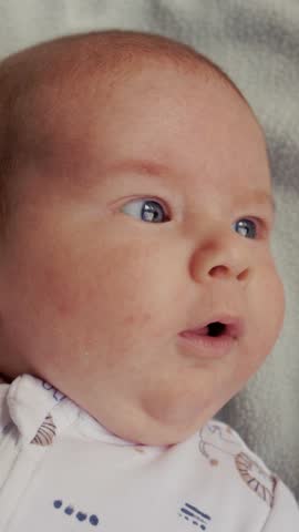 Close-up of a cute newborn baby boy with blue eyes looking around and making funny faces