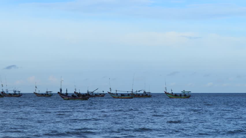 A group of wooden fishing boats anchored off the north coast of Tuban, East Java, Indonesia at dusk.