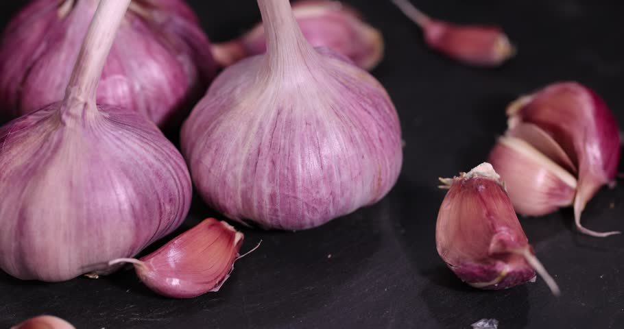 ripe purple garlic scattered on a black table in the kitchen and cloves of crushed garlic , garlic spices lie on a black board in the kitchen over cooking
