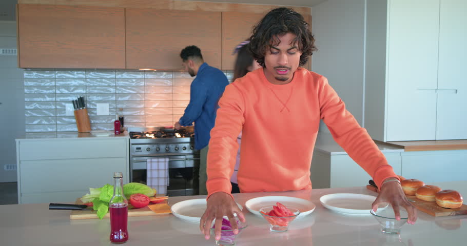 Diverse friends placing plates triggers cutting buns, lettuce, flipping patties for burgers at home. Cooking, teamwork, hospitality, modernkitchen, casual, foodpreparation, friendship
