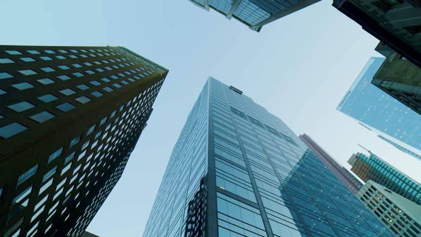 Dynamic rotating shot looking up at modern glass office towers in downtown Toronto, Canada. Low-angle perspective emphasizing height, corporate architecture, and urban business district skyline.