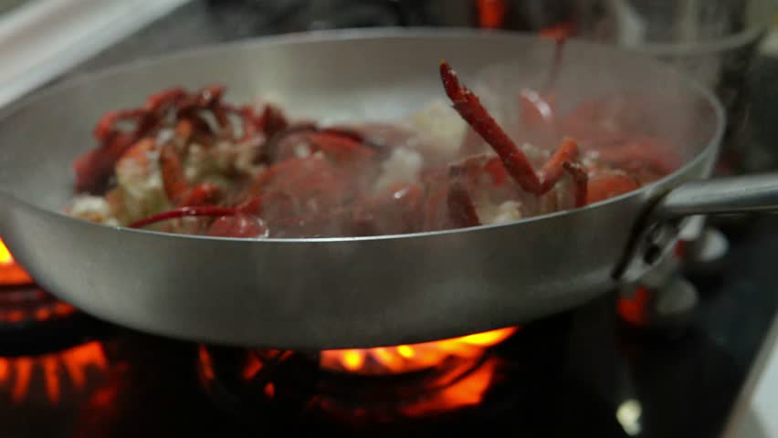 A high flame rises above the pan, searing the lobster shells. A professional chef flambés a lobster in a pan.