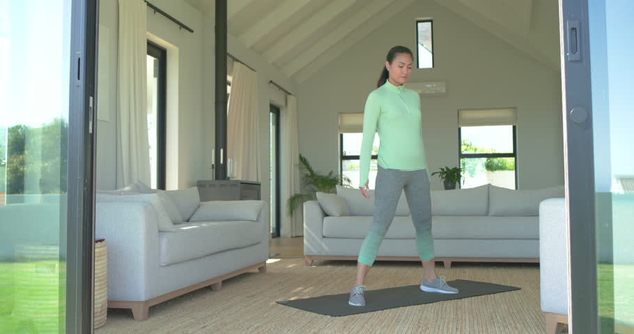 Asian woman at home lifting chest, arms overhead then folding on black yoga mat for flexibility. Wellness, flexibility, stretching, yoga, home fitness, serenity, relaxation