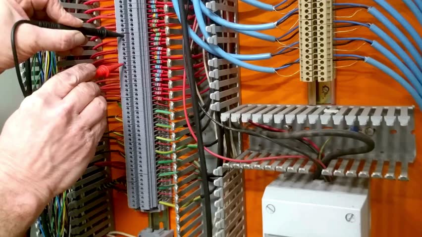 Hands working on electrical wiring in a control panel with colorful cables and connectors in high definition
