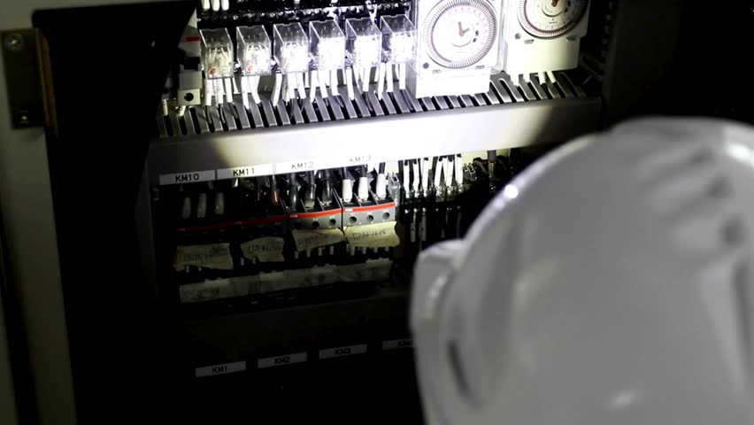 Electrician inspecting control panel in industrial setting during evening hours in high-definition