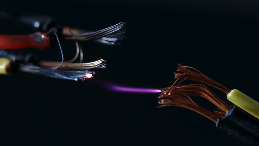 Electric discharge occurs in a dark setting as wires emit visible sparks and light in high-definition quality