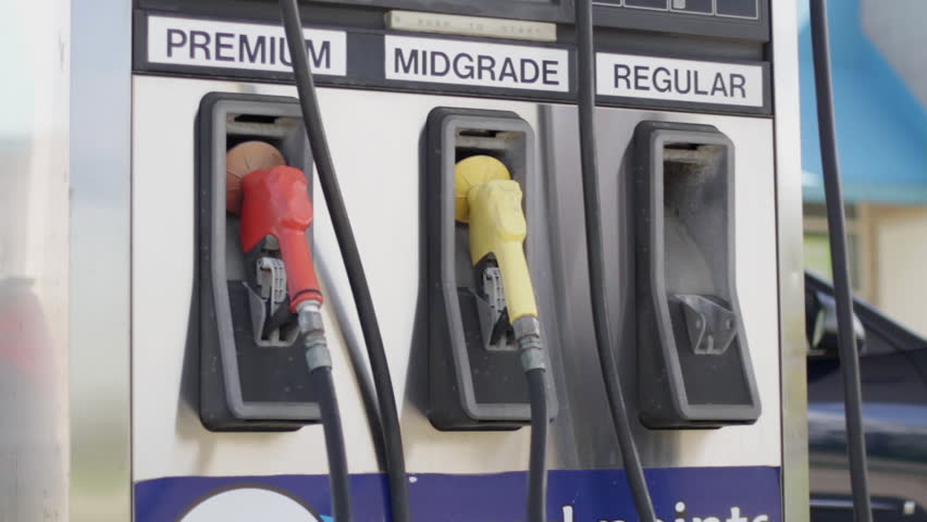 Man's hand selects regular fuel at a gas pump, then replaces the pump later in