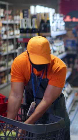 Asian busy shop assistant arranging foods on shelves collecting lettuce in grocery store. Chinese seller guy with face mask using tablet computer at organic supermarket.