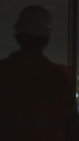 A man in a hard hat stands by a window, reflecting in darkness