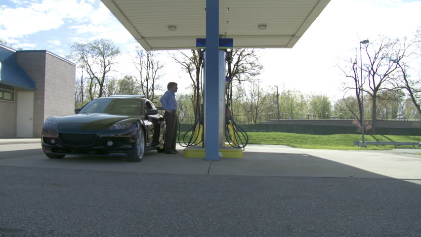 Two motorists fill up their cars at an unbranded self-service gas station.  Wide