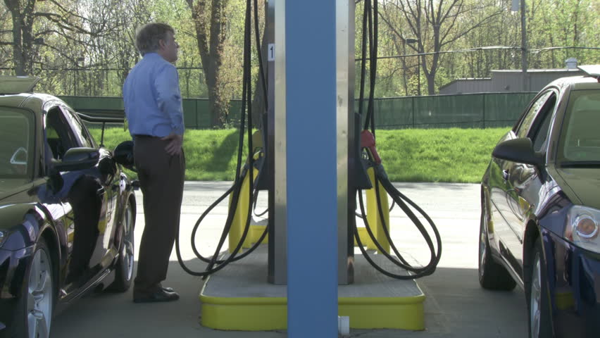 Two motorists fill up their cars at a self-service gas station.  Full length