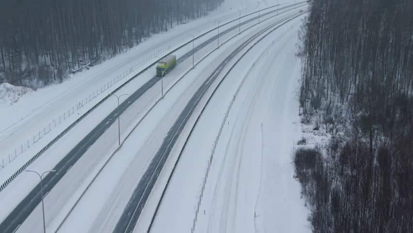 An overhead view of truck skillfully negotiating slippery icy curve amidst wooded landscape during winter
