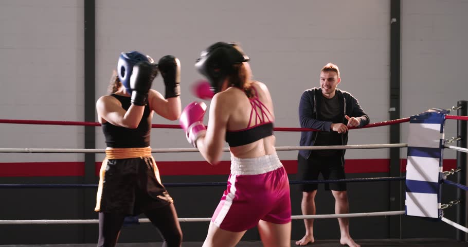 Female boxers sparring jabs under lights before coach stepping into ring and instructing punches. Training, fitness, aggression, focus, gym, competition, discipline