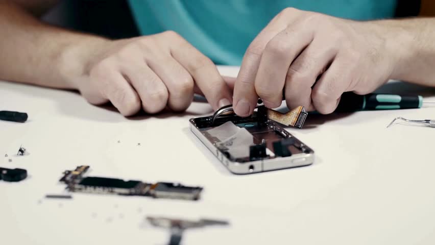 Close-up of hands skillfully disassembling a smartphone, surrounded by intricate components and tools, highlighting the precision of modern technology repair in a bright, organized workspace.