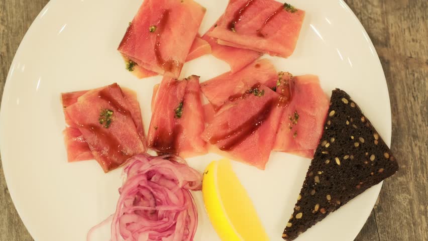 Tuna stroganina with pickled onion, lemon wedge, and rye bread on a white plate. Fresh seafood for gourmet dining, top view.