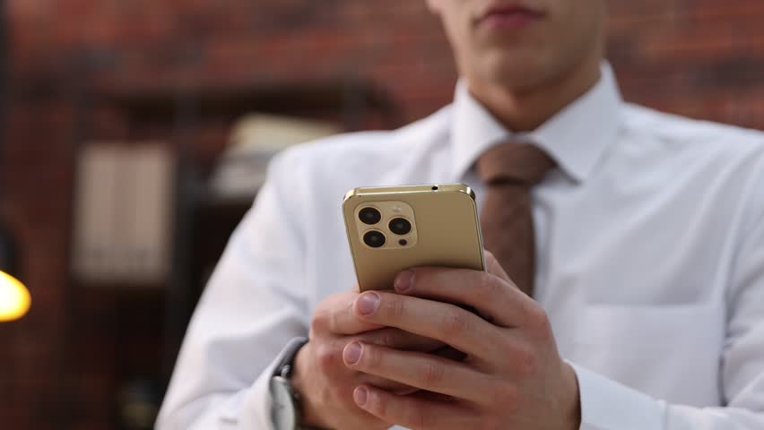 Man sending text message via smartphone indoors, closeup. Camera moving right