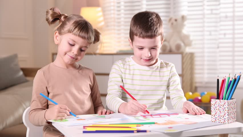 Little brother and sister drawing together at table indoors