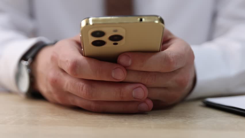 Man sending text message via smartphone at table indoors, closeup