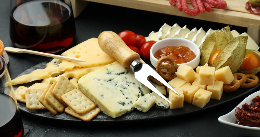 Woman taking piece of cheese from charcuterie board at black table, closeup