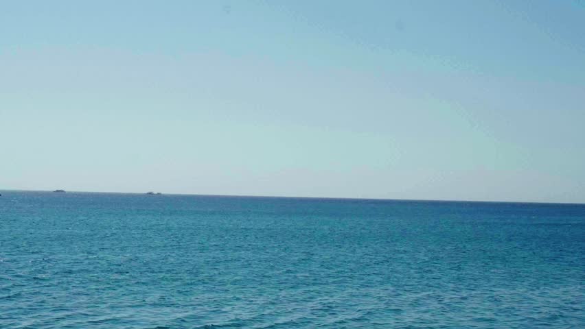 A calm summer landscape featuring a colorful rainbow arching over the blue ocean horizon with peaceful waves and clouds at a sunny tropical island beach vacation on a red sea of the gulf of agaba dahab