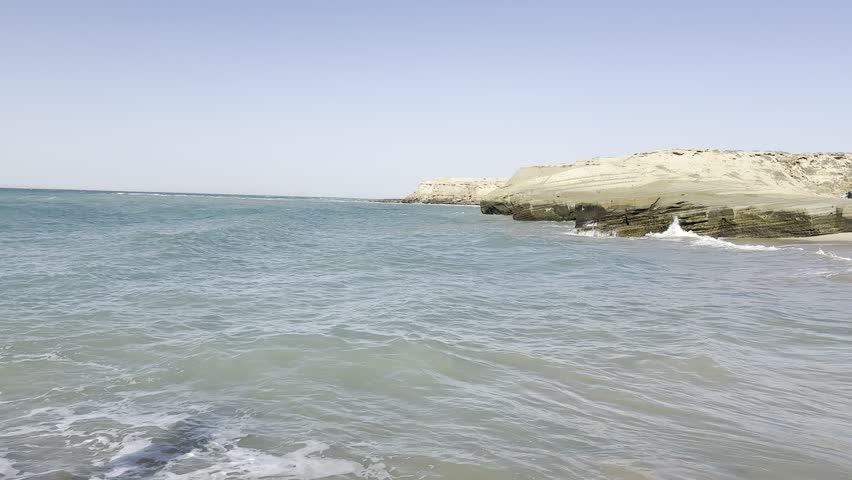 Wavy sea near rocky coastline with wind-driven waves on a sunny day, blue water and coastal landscape with copy space.
