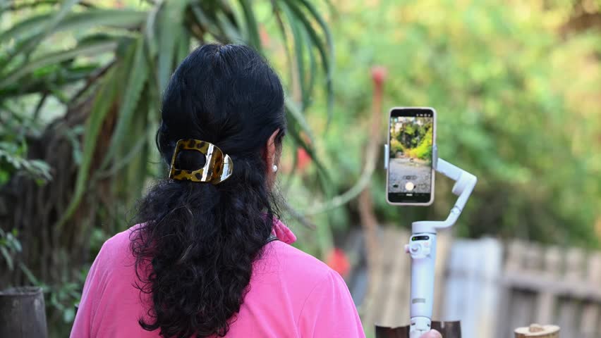 Close-up of a woman from behind using a smartphone stabilizer at a zoo