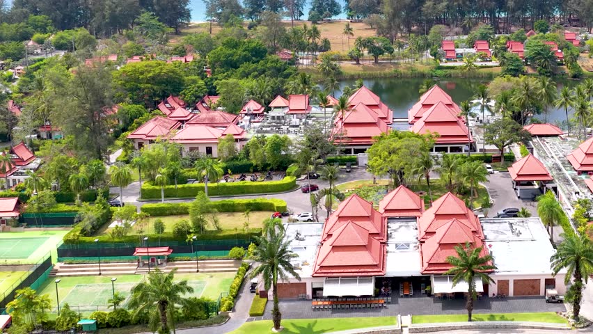 Drone footage pans across a luxury resort with red roofs, lush greenery, and calm lake