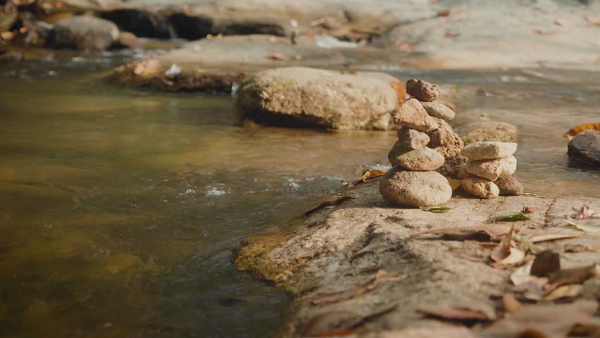 Stacked stones on flat river rock with flowing stream and earthy tones. Peaceful natural landscape symbolizing balance, mindfulness, solitude and harmony in nature.