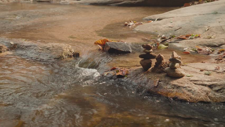 Stacked stones on flat river rock with flowing stream and earthy tones. Peaceful natural landscape symbolizing balance, mindfulness, solitude and harmony in nature.