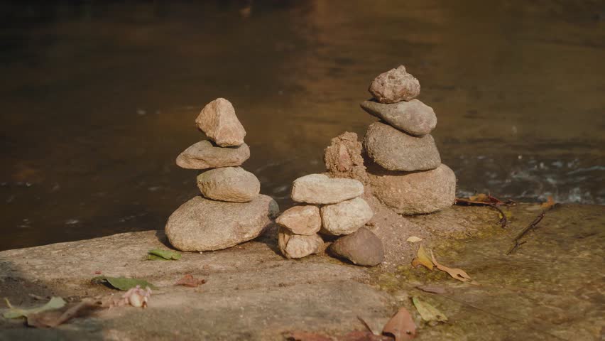 Stacked stones on flat river rock with flowing stream and earthy tones. Peaceful natural landscape symbolizing balance, mindfulness, solitude and harmony in nature.