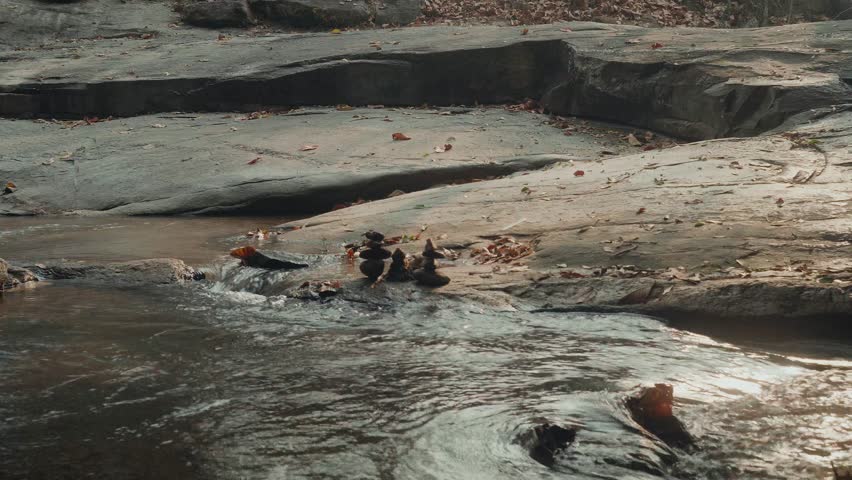 Stacked stones on flat river rock with flowing stream and earthy tones. Peaceful natural landscape symbolizing balance, mindfulness, solitude and harmony in nature.