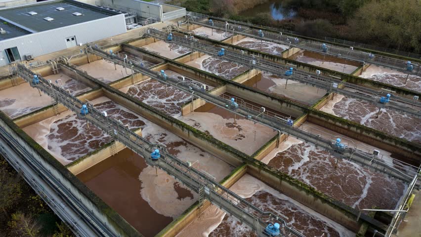 Aerial shot of a wastewater treatment plant in the United Kingdom with multiple processing tanks.