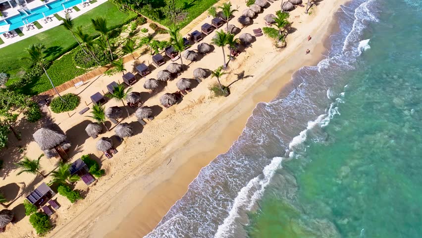 A sunny paradise with beach umbrellas on a sandy beach and blue sea. A popular summer tourist destination. Palm-fringed resort beaches of a Caribbean island. Summer travel concept. Seaside vacation.