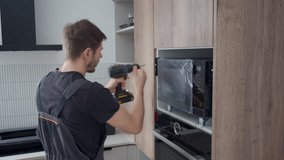 Man using cordless screwdriver to fixing new built in microwave oven with screws in modern kitchen cabinet. Concept of home appliances installing - Powered by Shutterstock - Get 15% off with code: PIKWIZARD15