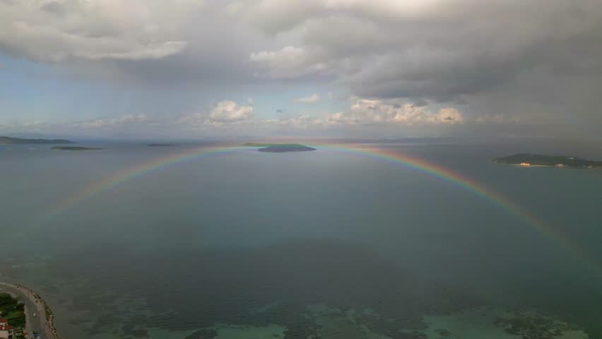 Vivid Rainbow Over Ocean Scene. Spectacular Rainbow Spans Turquoise Waters With Storm Clouds Behind