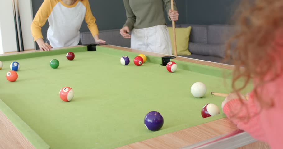After cue stick striking white ball, diverse female friends cheering in lounge by green-felt table. Recreation, socializing, leisure, urban, vibrant, playful, teamwork