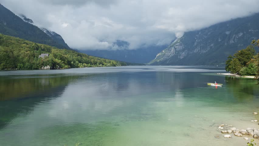 Group of kayakers paddling on Lake Bohinj under dramatic overcast summer sky in Slovenia, adventure and outdoor recreation. 4K selective focus.