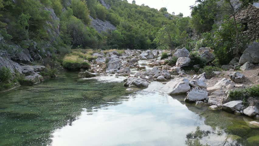 Low-altitude aerial flight over fast river rapids and flowing water in a canyon.