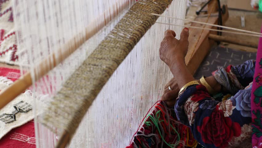Berber woman weaving traditional carpet on wooden loom, hands tying colorful threads. Close-up of artisan craftsmanship and textile production in Morocco and Tunisie
