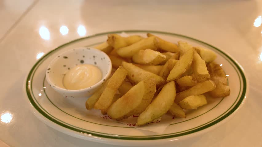 Close-up shot of a hand picking a potato wedge and dipping it into mayonnaise sauce
