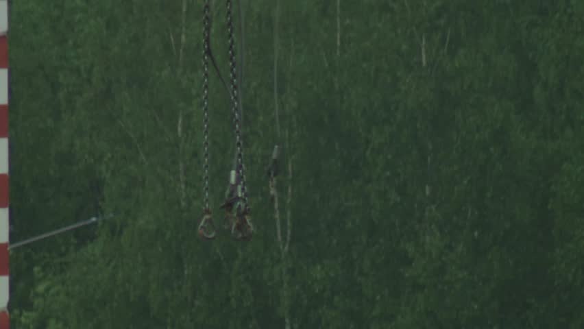 Close up view of metal chains and large hooks, part of a lifting crane mechanism. Lush green forest provides natural background. Scene depicts heavy construction equipment for slab house building.