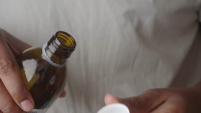 Pouring liquid medicine from brown bottle into white cap for dosage measurement motion