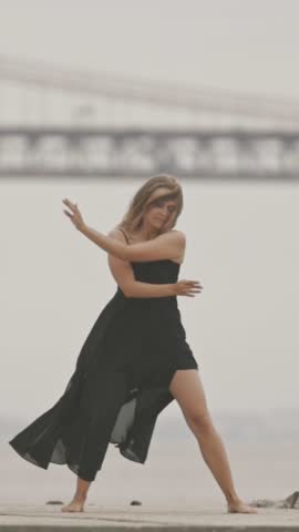 A woman in black dress dancing ballet on the pier in slow motion
